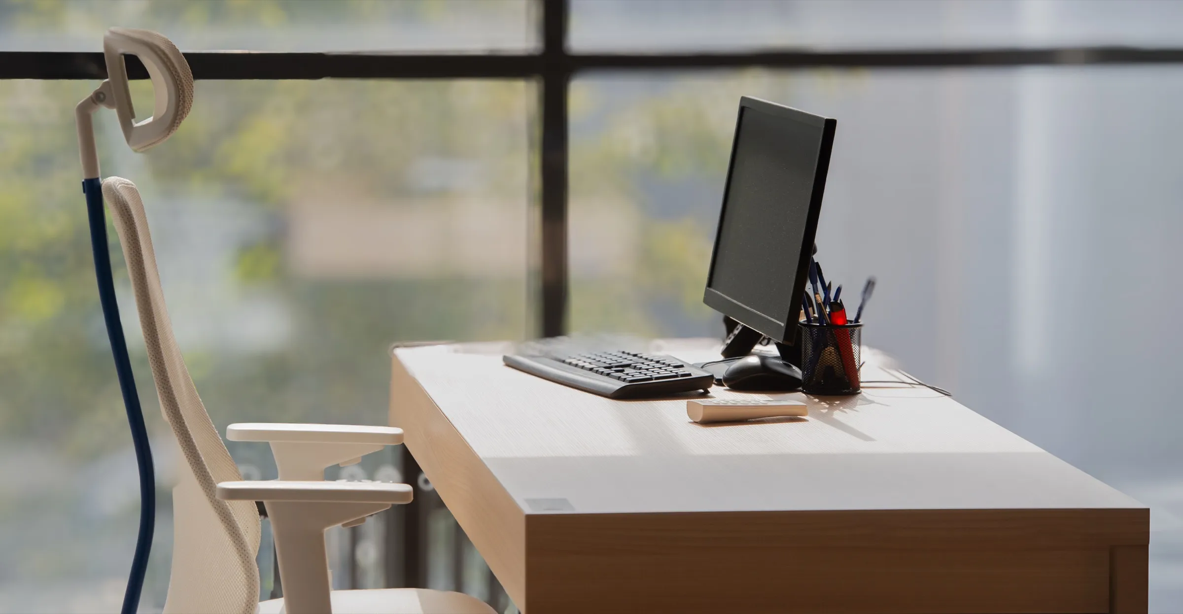 An empty desk by a window with a monitor, keyboard and office chair, set up and unoccupied